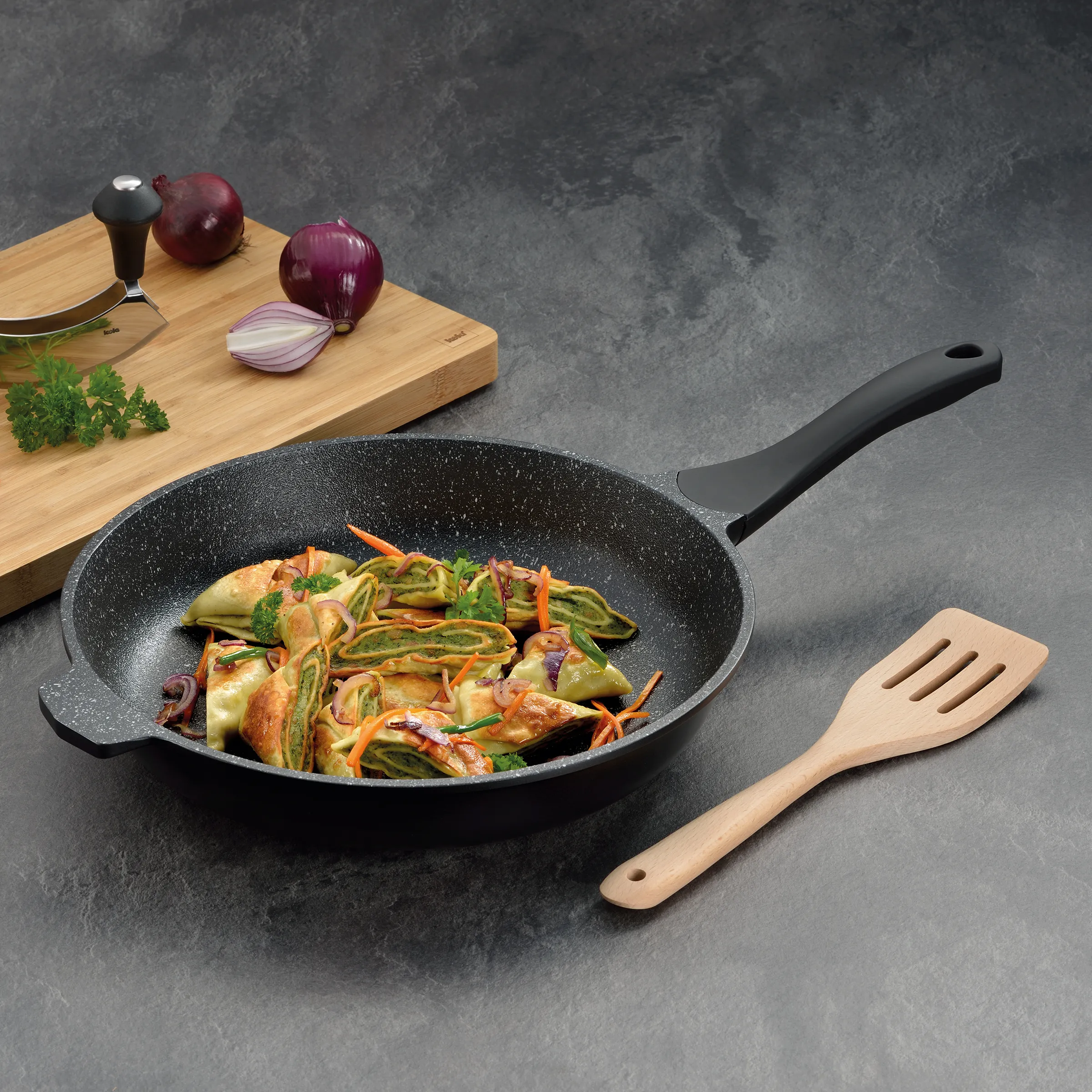Granitbeschichtete Bratpfanne mit gesundem Gemüse und asiatischen Dumplings Granitbeschichtete Bratpfanne mit Gemüse und Dumplings, Holzbrett mit roten Zwiebeln und Pfeffermühle