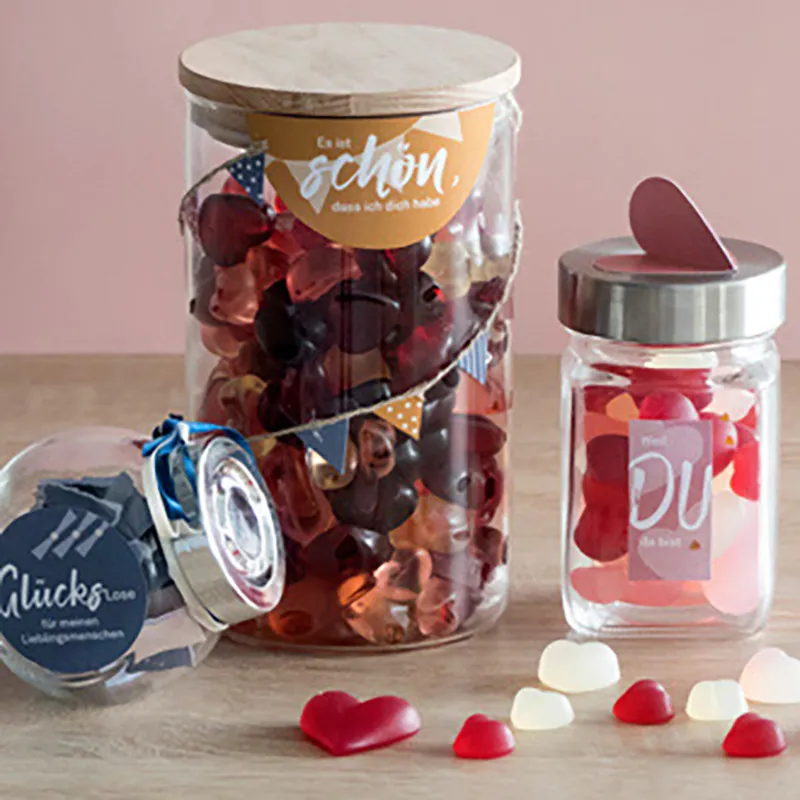 Ensemble Pots Verre Cœurs - Idée Cadeau Romantique Trois pots en verre remplis de cœurs rouges et blancs, avec des rubans et des étiquettes cadeaux