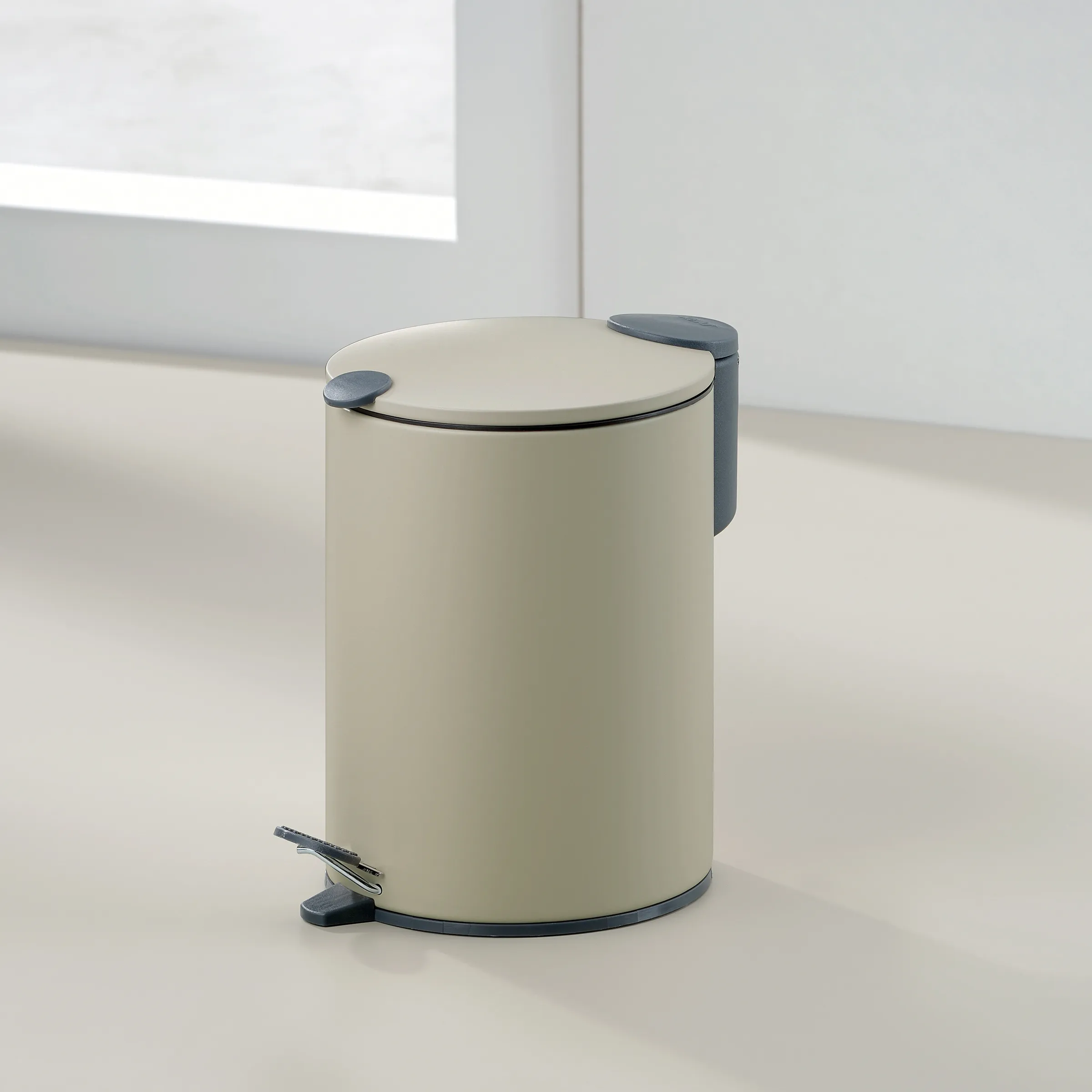 Beiger Tretmülleimer mit dunkelgrauem Pedal und Deckelgriff in minimalistischem Raum