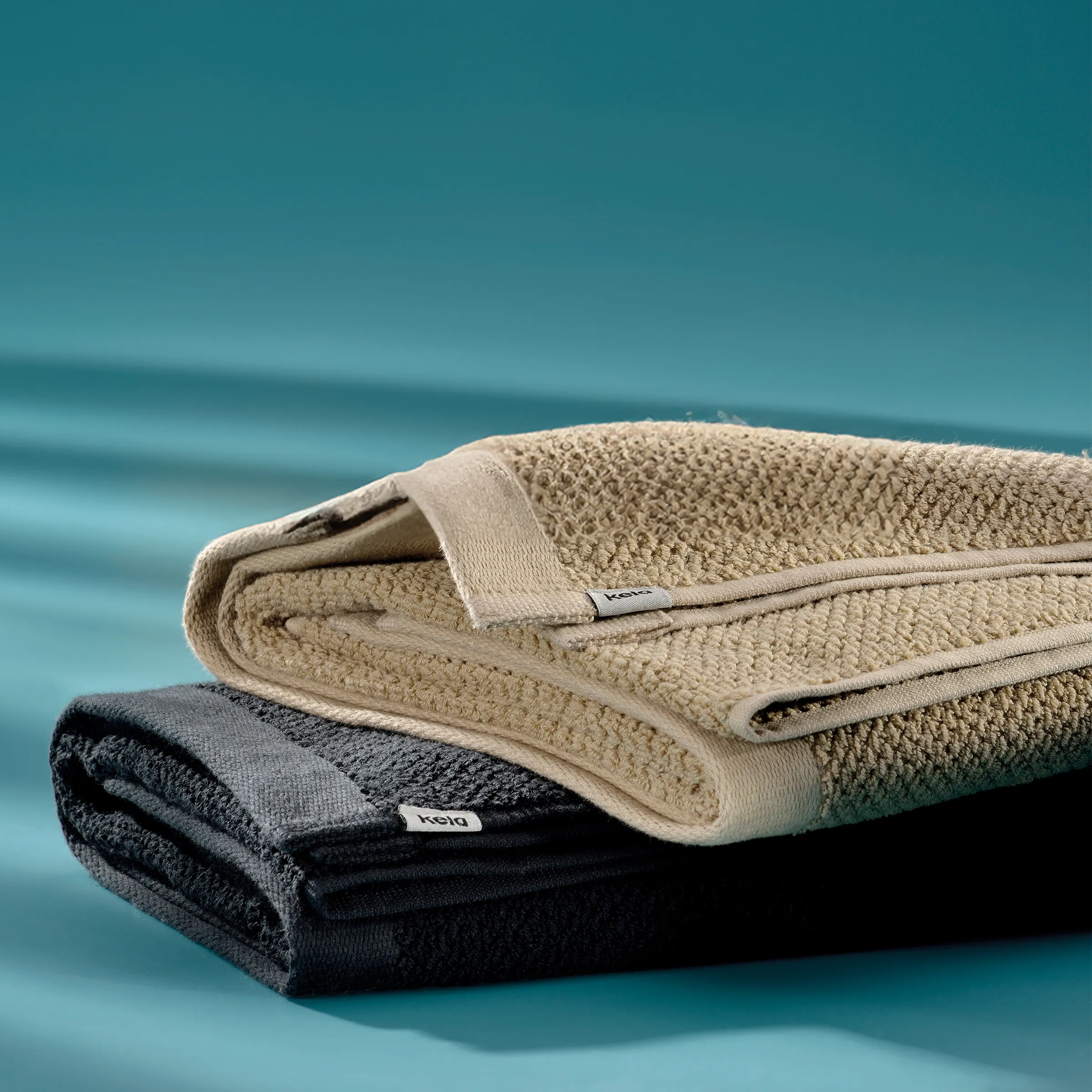 Premium Baumwoll-Handtücher in Beige und Blau – hochwertige Badetücher Zwei übereinander gestapelte Handtücher aus Baumwolle in Beige und Dunkelblau mit Strukturmuster auf türkisblauem Hintergrund