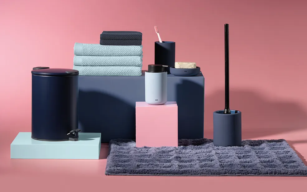Premium Badezimmer Accessoires Set - Handtücher & Behälter Badezimmer-Accessoires in Schwarz, Blau und Rosé: Behälter, Handtücher, Zahnbürstenhalter und Klobürste auf rosa Hintergrund