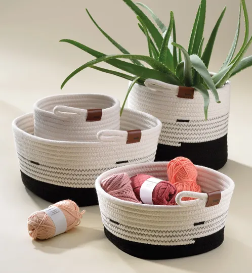 Baumwoll-Aufbewahrungskörbe Set mit Wollknäueln Vier Baumwoll-Aufbewahrungskörbe in Creme und Schwarz mit braunen Ledergriffen, gefüllt mit Wollknäueln und Pflanze