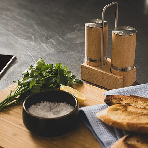 Salz- und Pfeffermühle aus Holz auf Schneidebrett mit Kräutern, Salz und geröstetem Brot