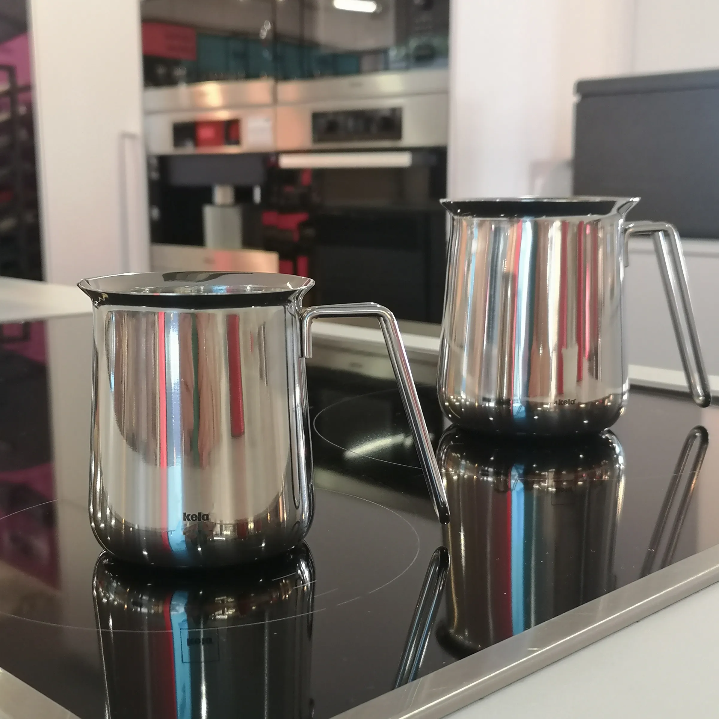 Edelstahl Milchkännchen Set - Professionelle Barista Kanne Zwei glänzende Edelstahl-Milchkännchen mit modernem Design auf schwarzer Küchenoberfläche