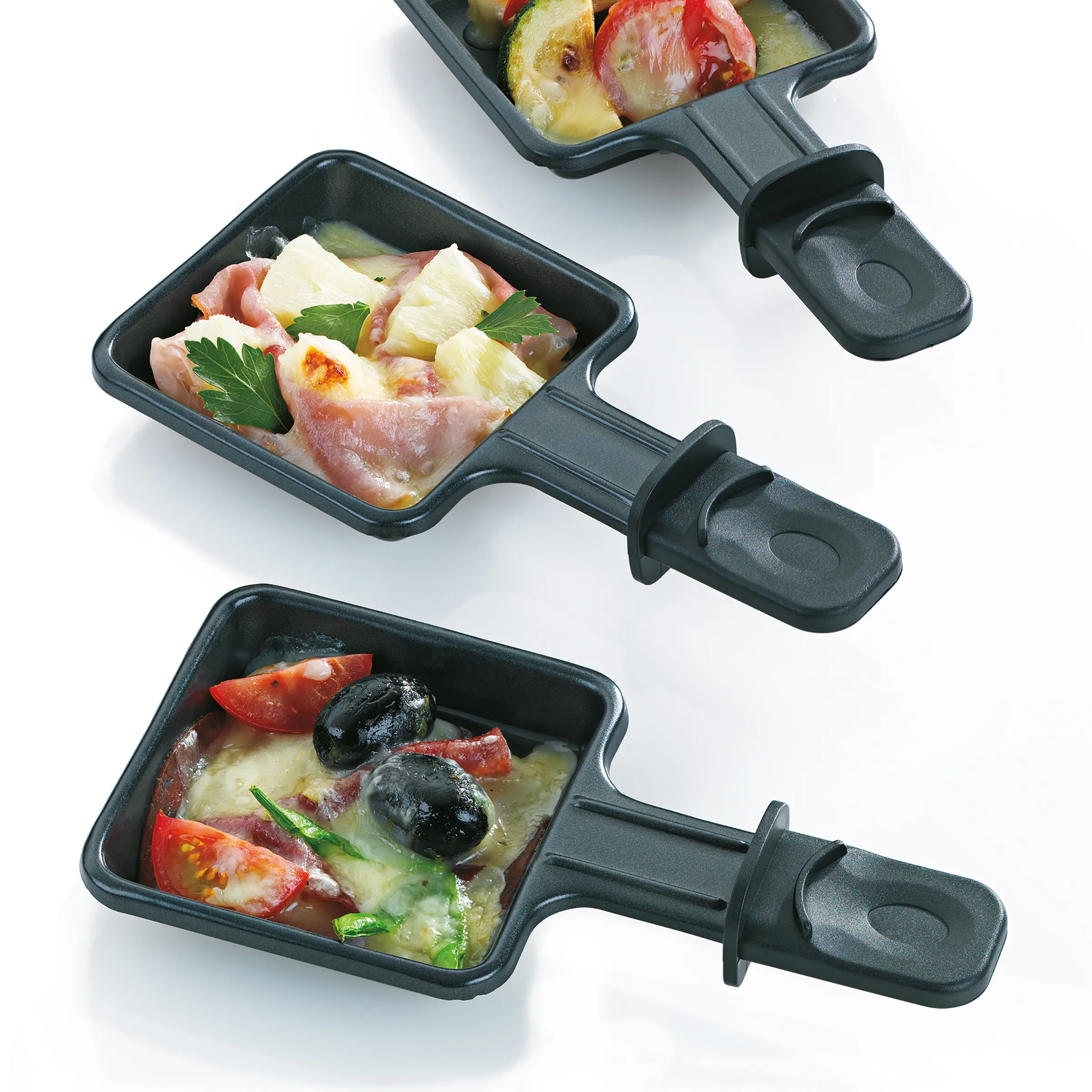 Raclette-Pfännchen mit Käse und verschiedenen Zutaten - Raclette Grillzubehör Drei Raclette-Pfännchen mit geschmolzenem Käse, Schinken, Tomaten, Oliven und Petersilie auf weißem Hintergrund