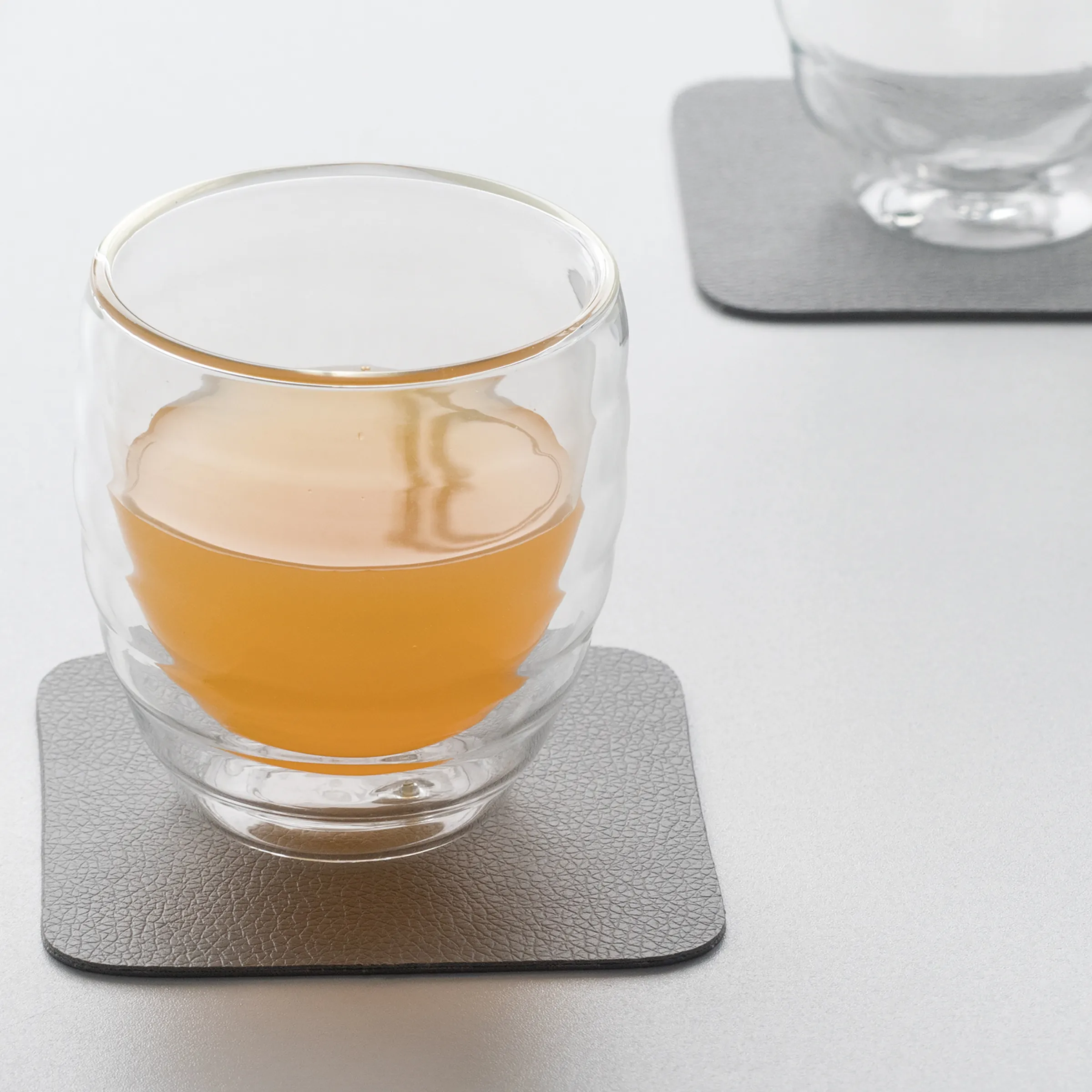 Doppelwandiges Glas mit Getränk und Untersetzer Doppelwandiges Glas mit goldenem Rand auf grauem Untersetzer, gefüllt mit bernsteinfarbenem Getränk