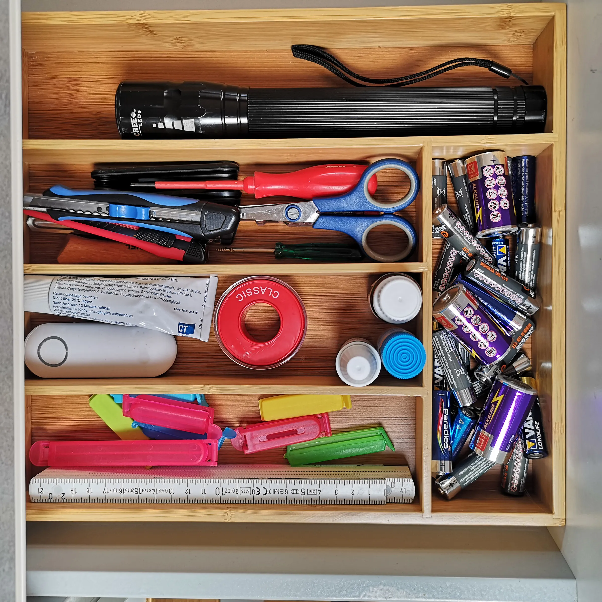 Werkzeug Organizer Schublade - Ordnung für Haushalt und Handwerk Holzschublade mit organisiertem Inhalt: Taschenlampe, Schere, Werkzeuge, rotes Klebeband, Batterien und Messstab