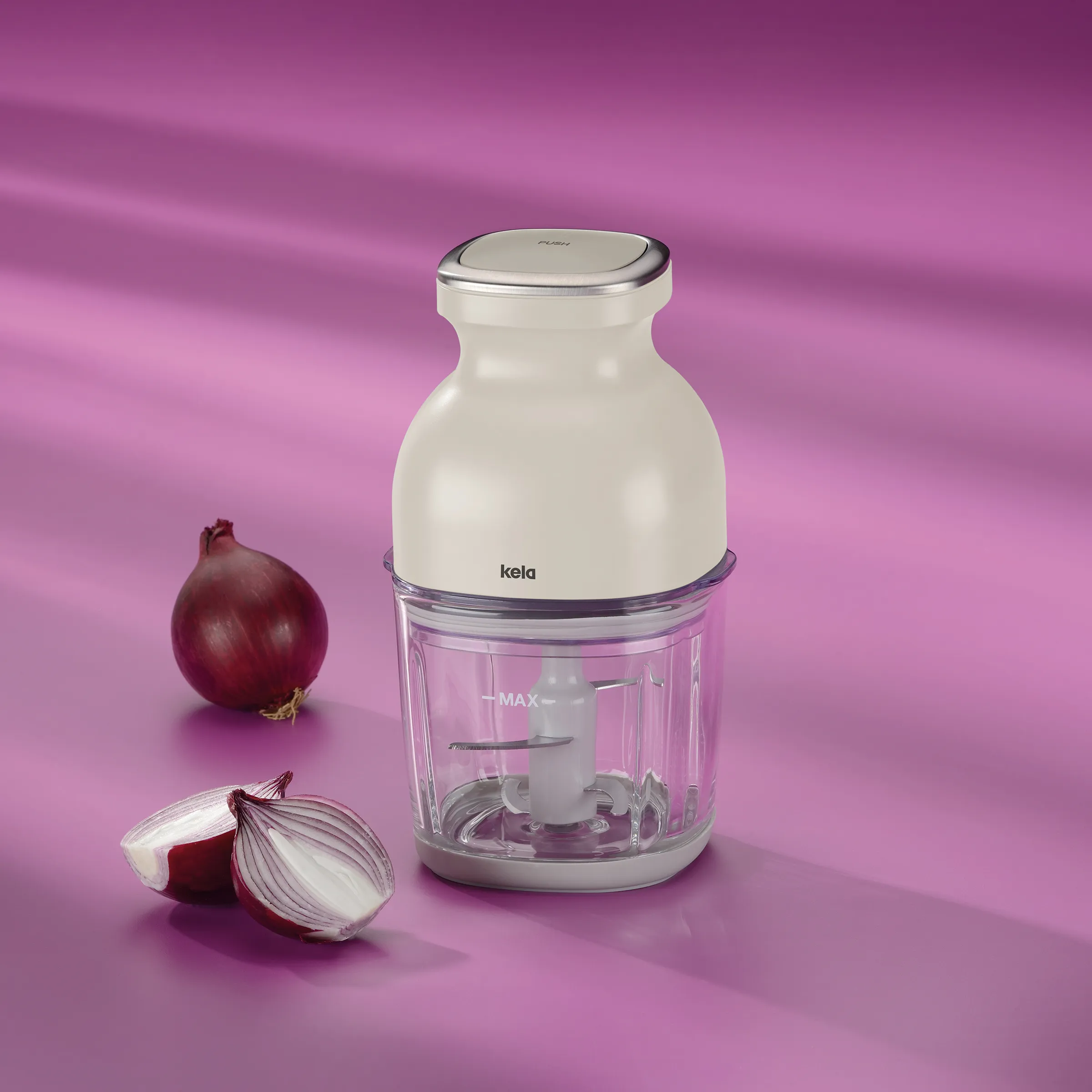 Kela Zwiebelschneider mit weißem Gehäuse und transparentem Behälter neben frischen roten Zwiebeln auf rosa Hintergrund