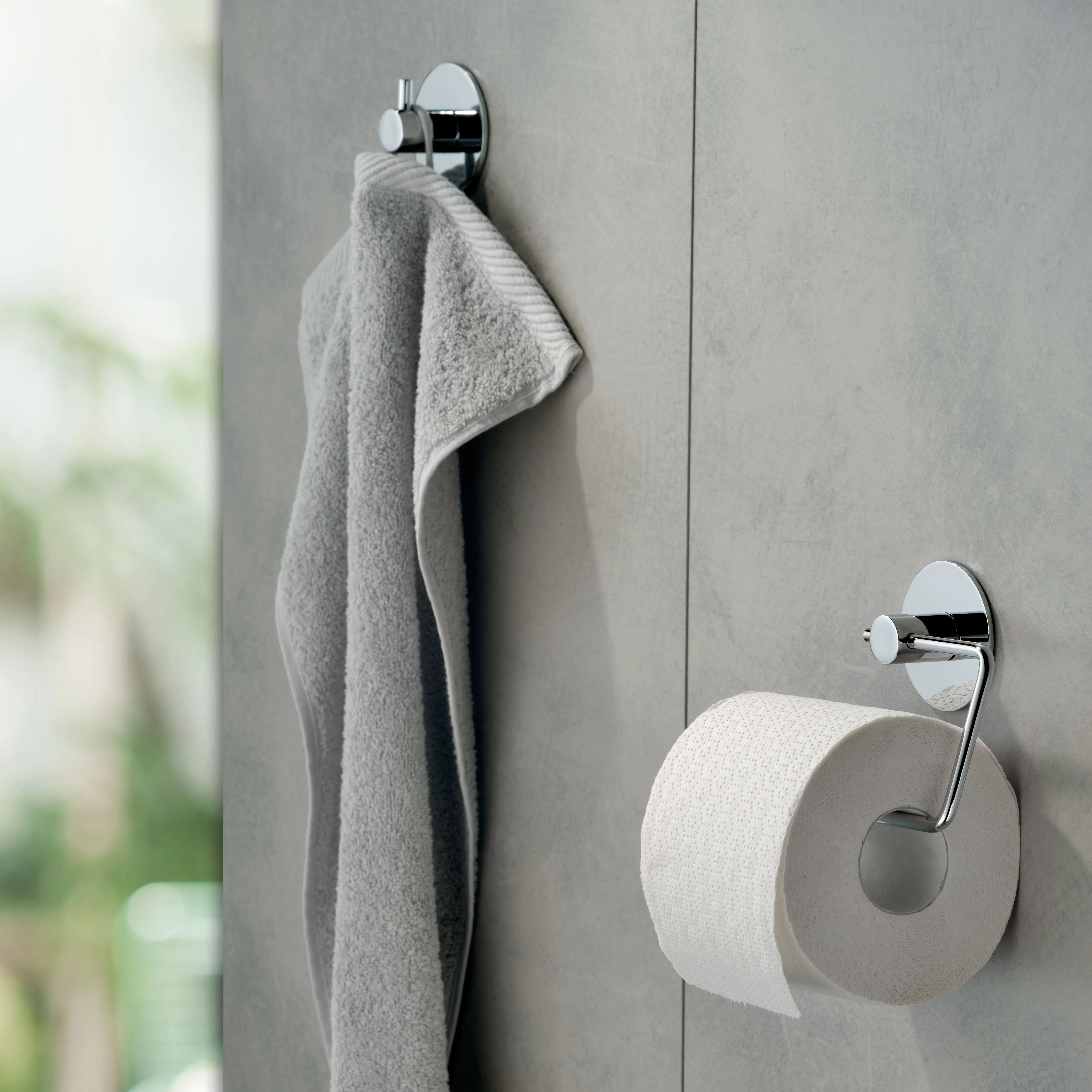 Chrom Handtuchhaken und Toilettenpapierhalter Set für modernes Badezimmer Chromhaken mit grauem Handtuch und Toilettenpapierhalter an grauer Badezimmerwand