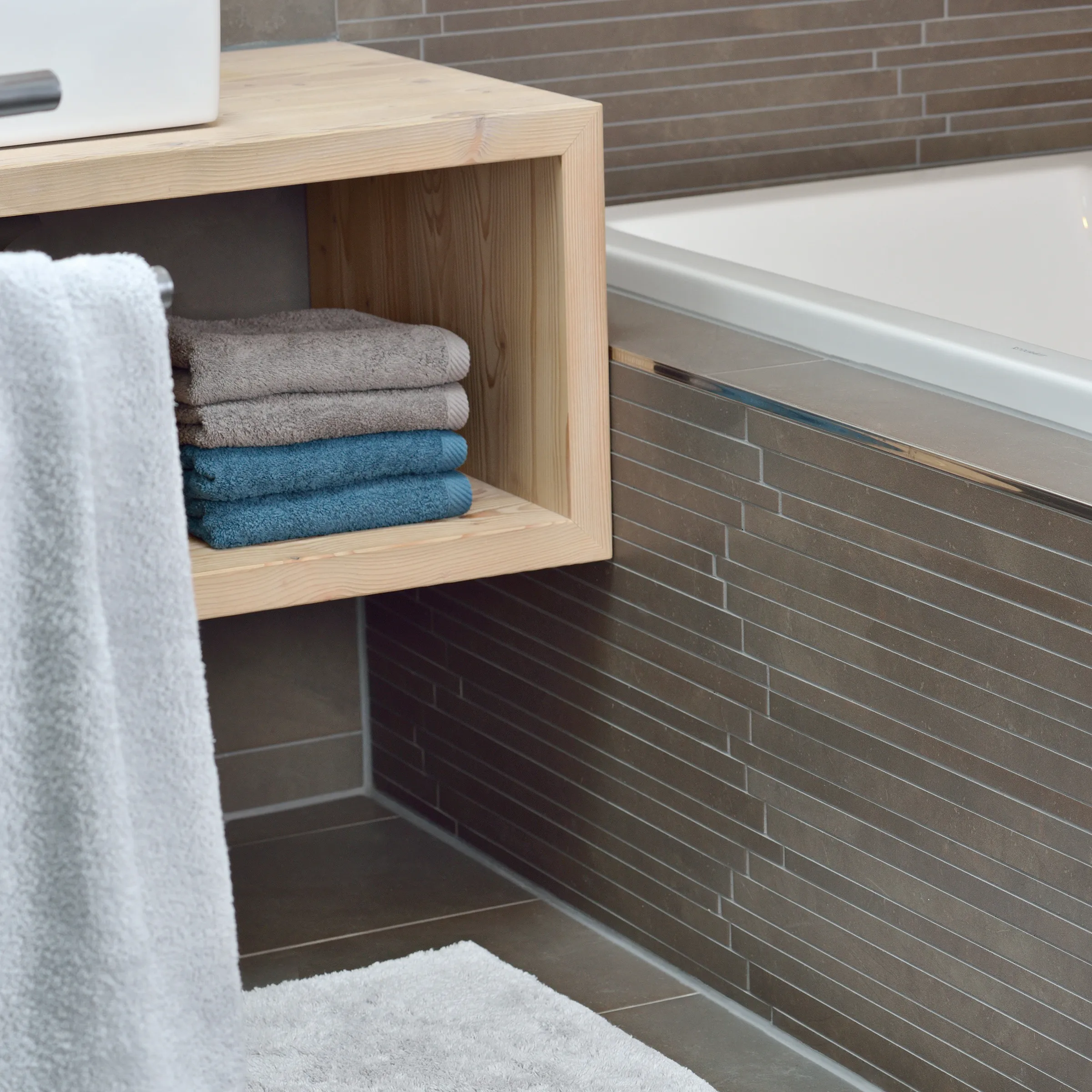 Badezimmer Organisation mit Holzregal und Handtücher Aufbewahrung Modernes Badezimmer mit Holzregal und gefalteten Handtüchern neben weißer Badewanne vor brauner Fliesenwand