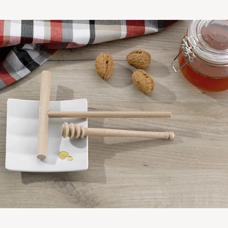 Honig-Dispenser Holz - praktisches Honigset Honig-Dispenser mit Holzstab auf weißem Teller, Mandeln, Honigwabe und Glas mit Honig auf Holztisch neben kariertem Tuch.