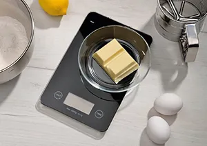 Digitale Küchenwaage zum Backen und Kochen Digitale Küchenwaage mit Butter, Eiern und Zutaten zur Vorbereitung eines Backrezepts