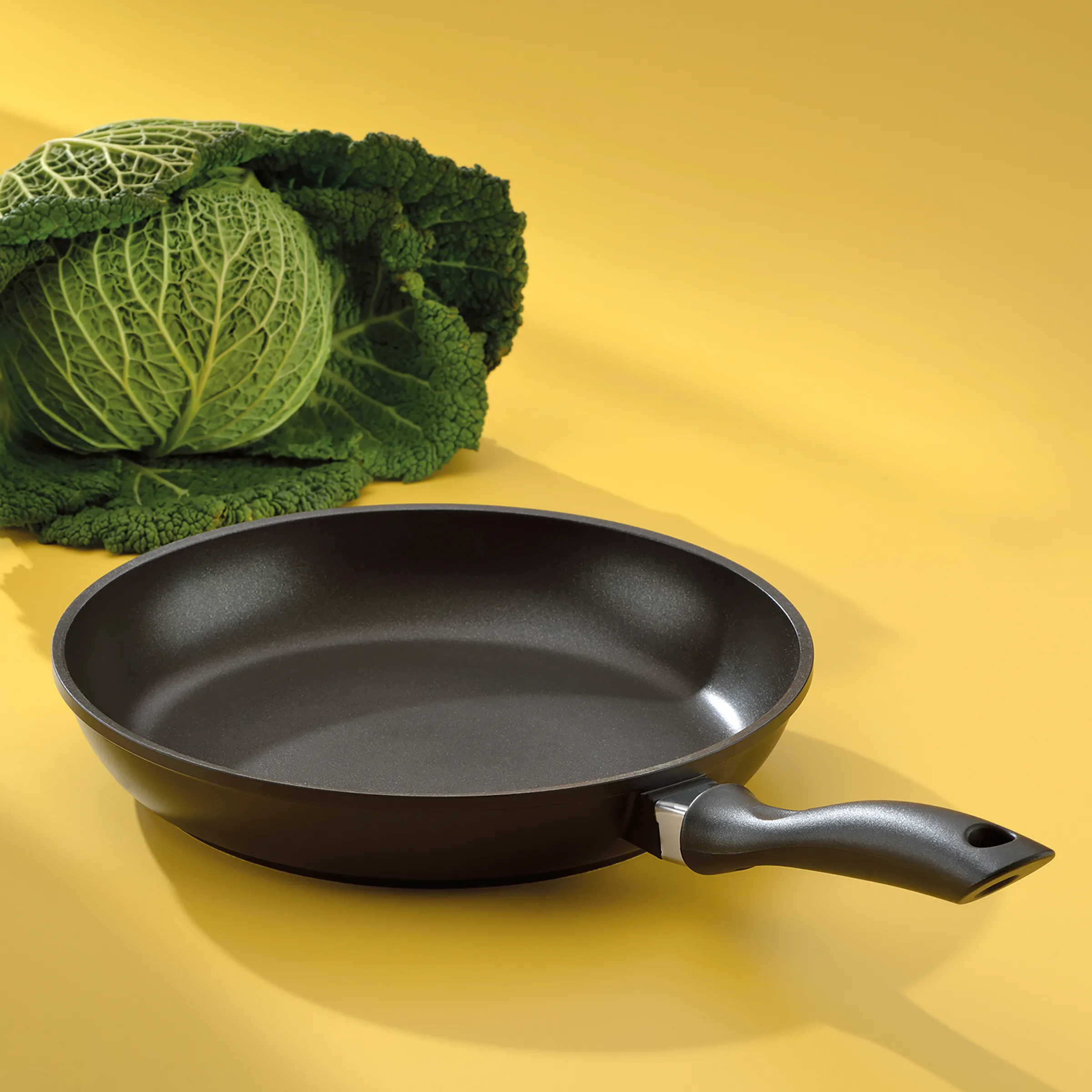 Antihaft-Bratpfanne und Kohl - Küchenzubehör Schwarze Antihaft-Bratpfanne mit grünem Kohlkopf auf gelbem Hintergrund