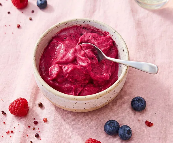 Himbeer Mousse Rezept - cremige Beeren Dessert Cremefarbene Schüssel mit intensiv pinkfarbener Himbeercreme oder Mousse, garniert mit frischen Himbeeren und Blaubeeren auf rosa Untergrund
