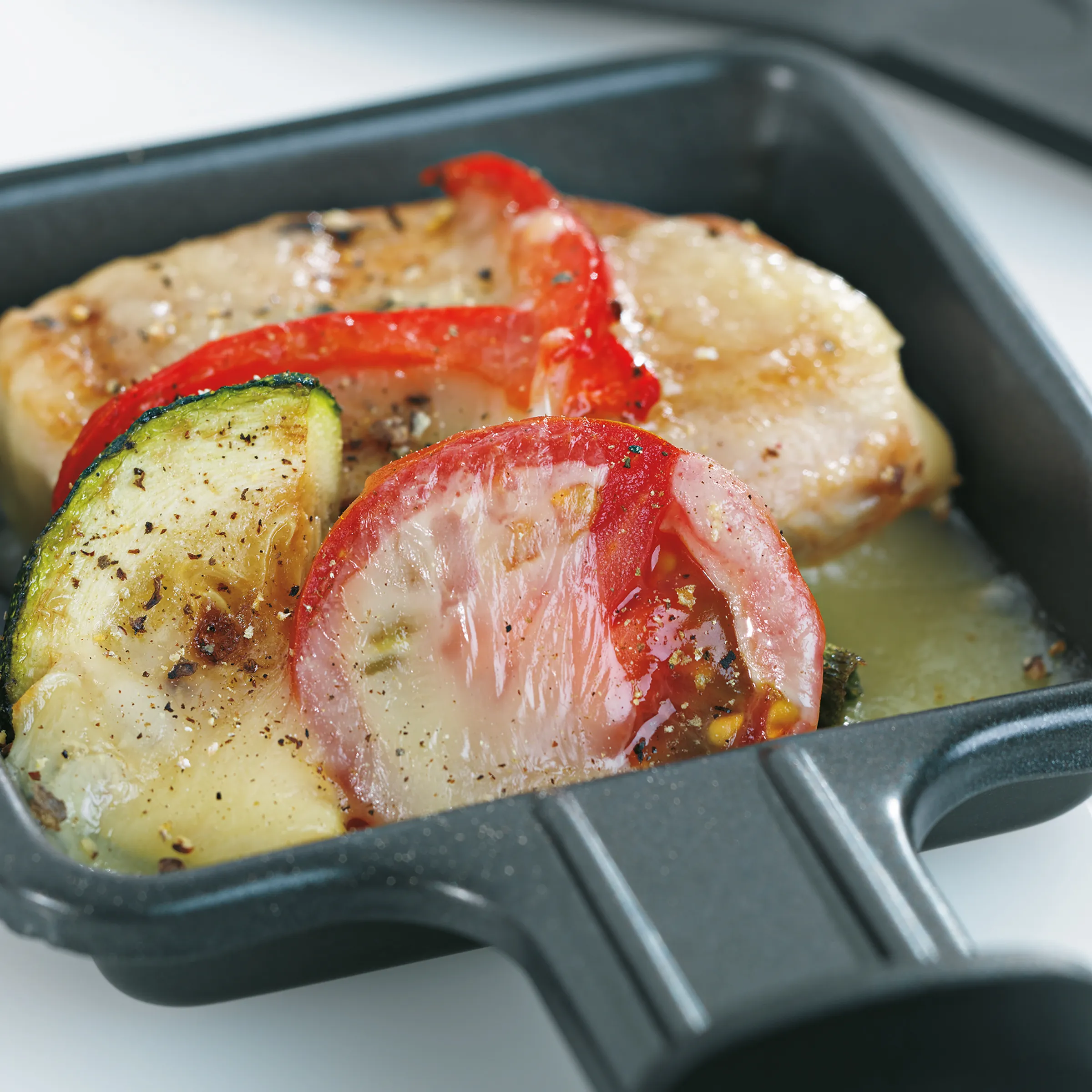 Raclette-Pfännchen mit Gemüse und Käse - Raclette-Rezept Raclette-Pfännchen mit geschmolzenem Käse, Zucchini, Tomaten und Paprika, gewürzt mit Pfeffer