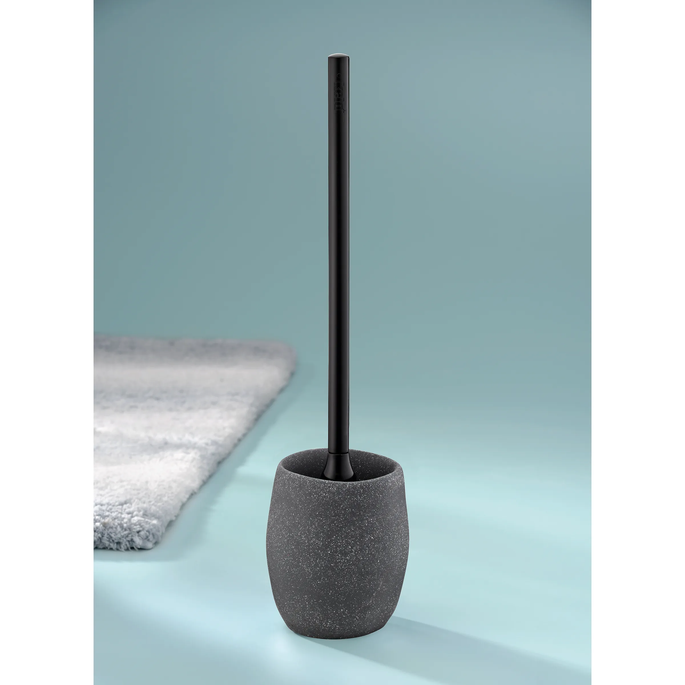 WC-Bürste mit Keramikhalter in Grau - Stilvolles Badezimmer-Accessoire Schwarze WC-Bürste mit grauem Keramikhalter auf blauem Untergrund neben weißem Handtuch