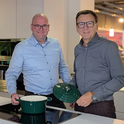 Gusseisen Kochtopf - Hochwertige Küchenkochware Zwei Männer mit Brille präsentieren einen grünen Gusseisen-Kochtopf mit Deckel in einer modernen Küche