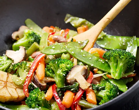 Gemüse Wok Stir-Fry Rezept mit Brokkoli und Paprika Wok mit Gemüse-Stir-Fry: Brokkoli, Paprika, Pilze und Zuckerschoten werden mit Holzlöffel in schwarzem Wok gerührt