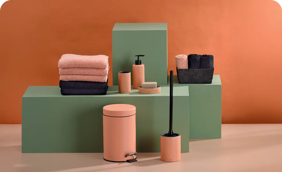 Rosa und schwarze Badezimmer-Accessoires mit Handtüchern auf grünen Podesten vor orangem Hintergrund