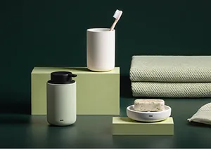 Minimalistische Badezimmer-Accessoires: zwei weiße Zahnbürstenhalter, grüne Boxen und gestapelte grüne Handtücher auf grauem Untergrund