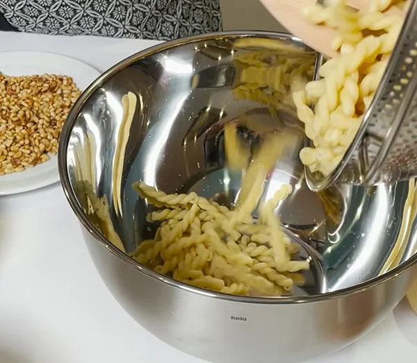 Käse reiben in Edelstahlschüssel - Küchenreibe und frisch geriebener Käse Geriebener Käse fällt von einer Reibe in eine Edelstahlschüssel, Sesam im Hintergrund