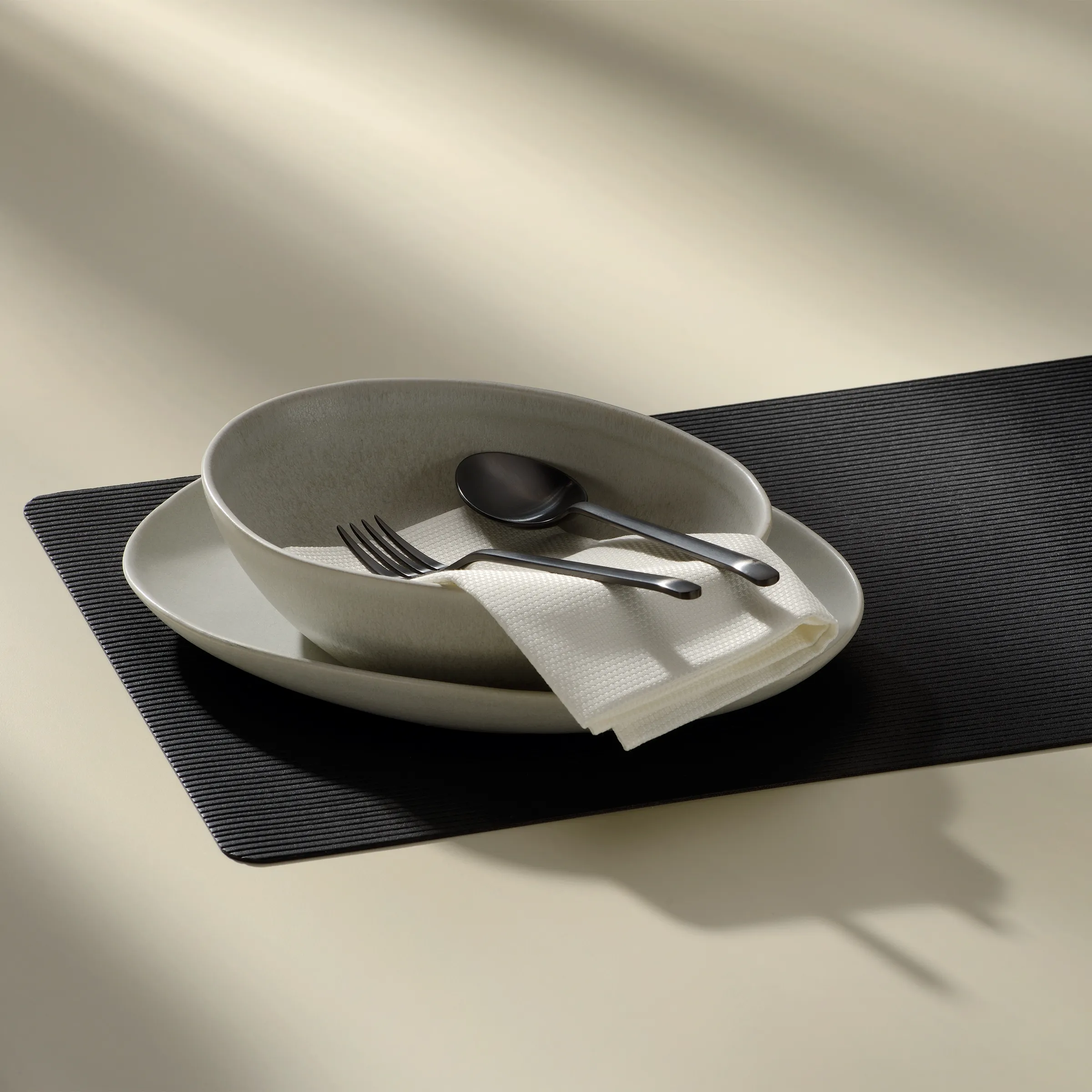 Moderne Tischeinstellung - Elegantes Besteck und Geschirr Elegante Tischeinstellung mit weißen Tellern, schwarzem Besteck und weißer Serviette auf schwarzem Platzdeckchen