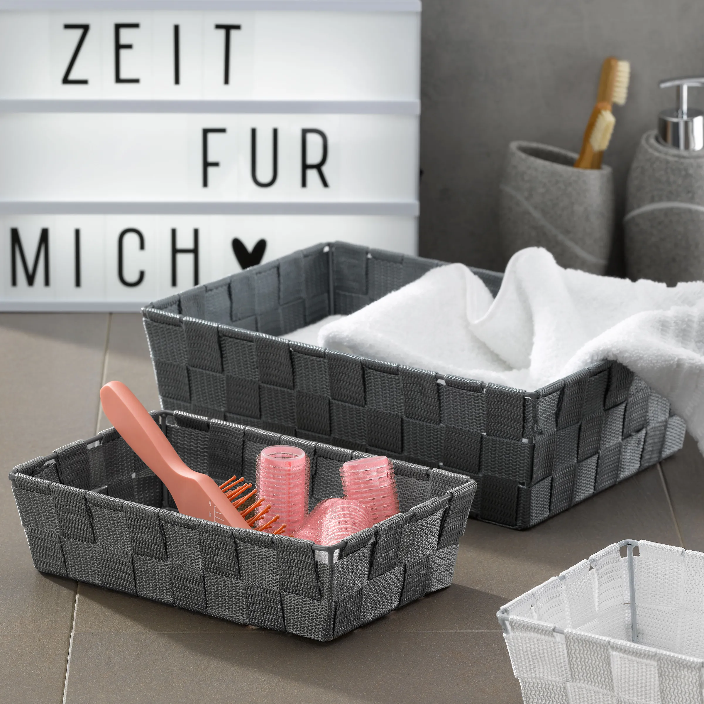 Geflochtene Aufbewahrungskörbe Bad - Badezimmer Organizer Set grau Graue geflochtene Aufbewahrungskörbe mit Handtüchern und Haarbürste neben Lightbox 'Zeit für mich'