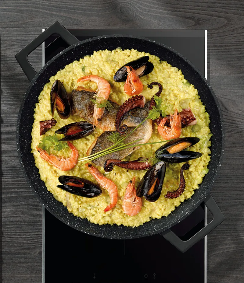 Seafood Paella - authentisches Meeresfrüchte-Reisgericht Paella in schwarzer Pfanne mit Meeresfrüchten: Garnelen, Muscheln, Fisch und Oktopus auf gelbem Safranreis mit frischen Kräutern