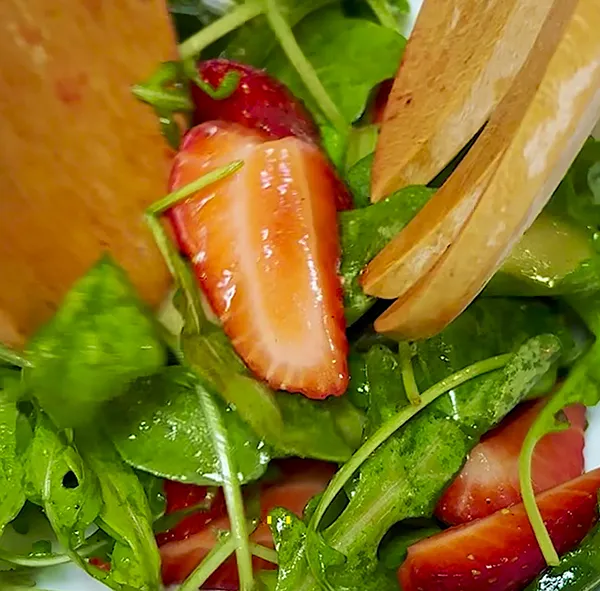 Rucola-Erdbeersalat mit Balsamico-Dressing - Frischer Sommersalat Frischer Rucola-Erdbeersalat mit Balsamico-Dressing und Parmesanscheiben auf weißem Teller