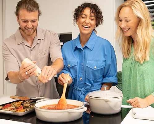 Kochen Gruppe Küche - Gemeinsames Kochen Drei Personen kochen gemeinsam in der Küche. Eine Person rührt in einem Topf, während die anderen lächelnd zusehen.