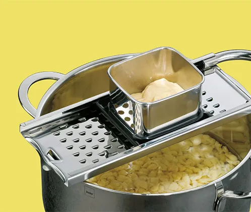 Nudelsieb Kartoffelpresse Edelstahl Küchenzubehör Nudelsieb und Kartoffelpresse aus Edelstahl auf gelbem Hintergrund mit gekochten Nudeln in Topf