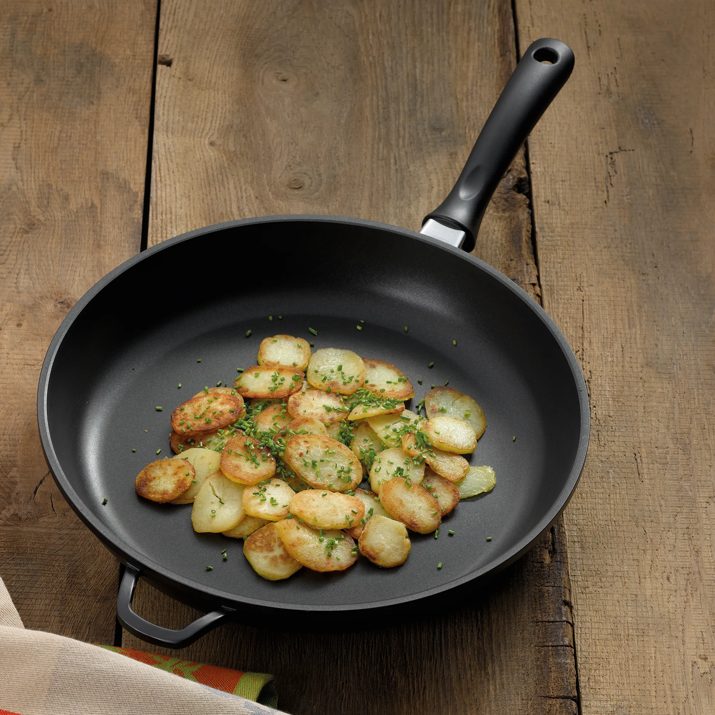 Gebratene Kartoffeln in der Pfanne - einfaches Rezept Schwarze Pfanne mit gebratenen Kartoffelscheiben, garniert mit frischen Kräutern auf Holztisch