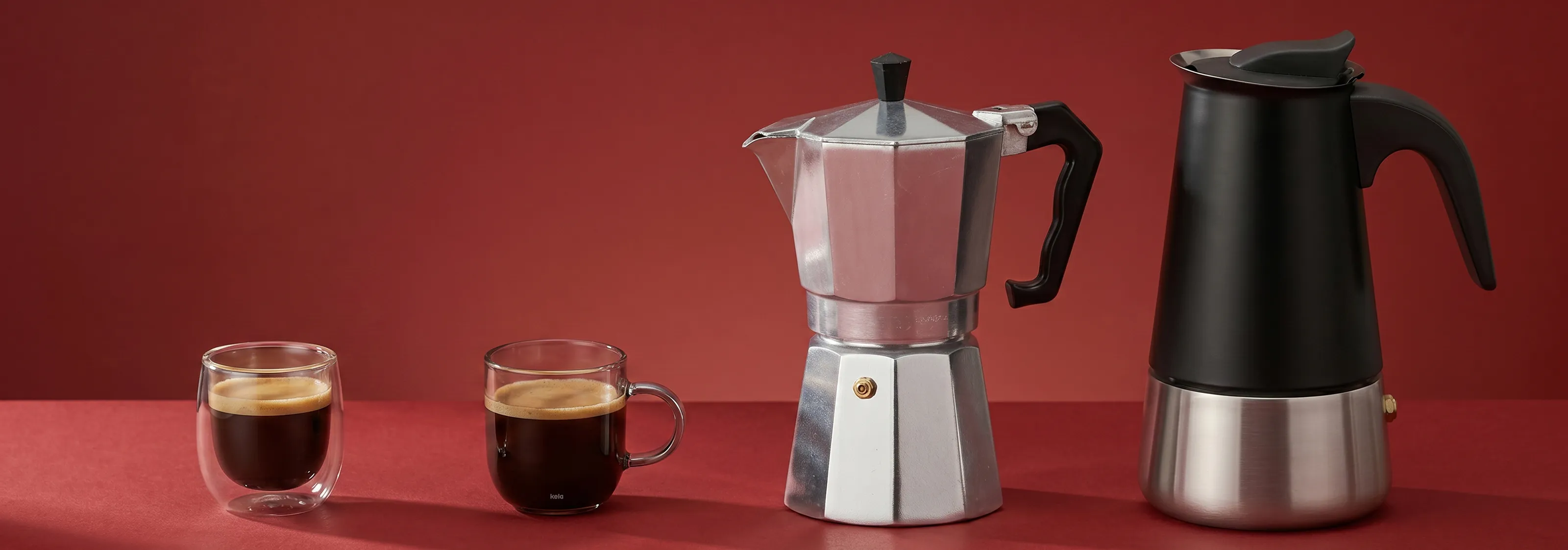 Espressokannen Set - Klassische und moderne Mokkakannen für perfekten Kaffeegenuss Zwei Espressotassen neben klassischer Aluminium-Espressokanne und moderner schwarzer Espressokanne auf rotem Hintergrund
