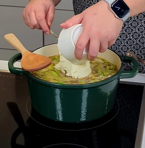 Sauerrahm in Suppe einrühren - Kochen im grünen Topf Person gibt Sauerrahm aus Becher in grünen Topf mit Suppe auf Herd, Holzlöffel sichtbar