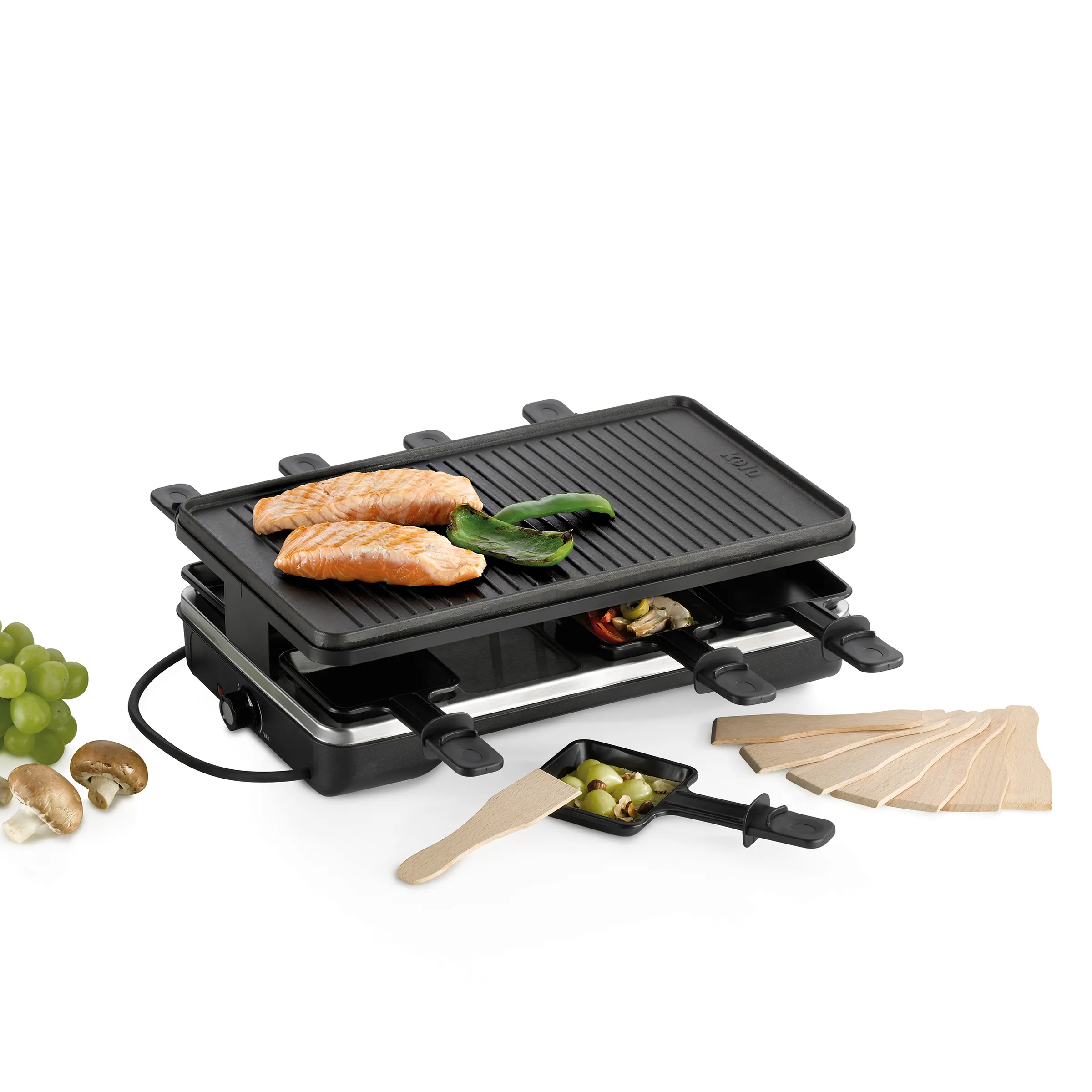 Raclette-Grill mit Grillplatte, zwei Fischfilets und Paprika, begleitet von Holzspachteln, Pilzen und Trauben.