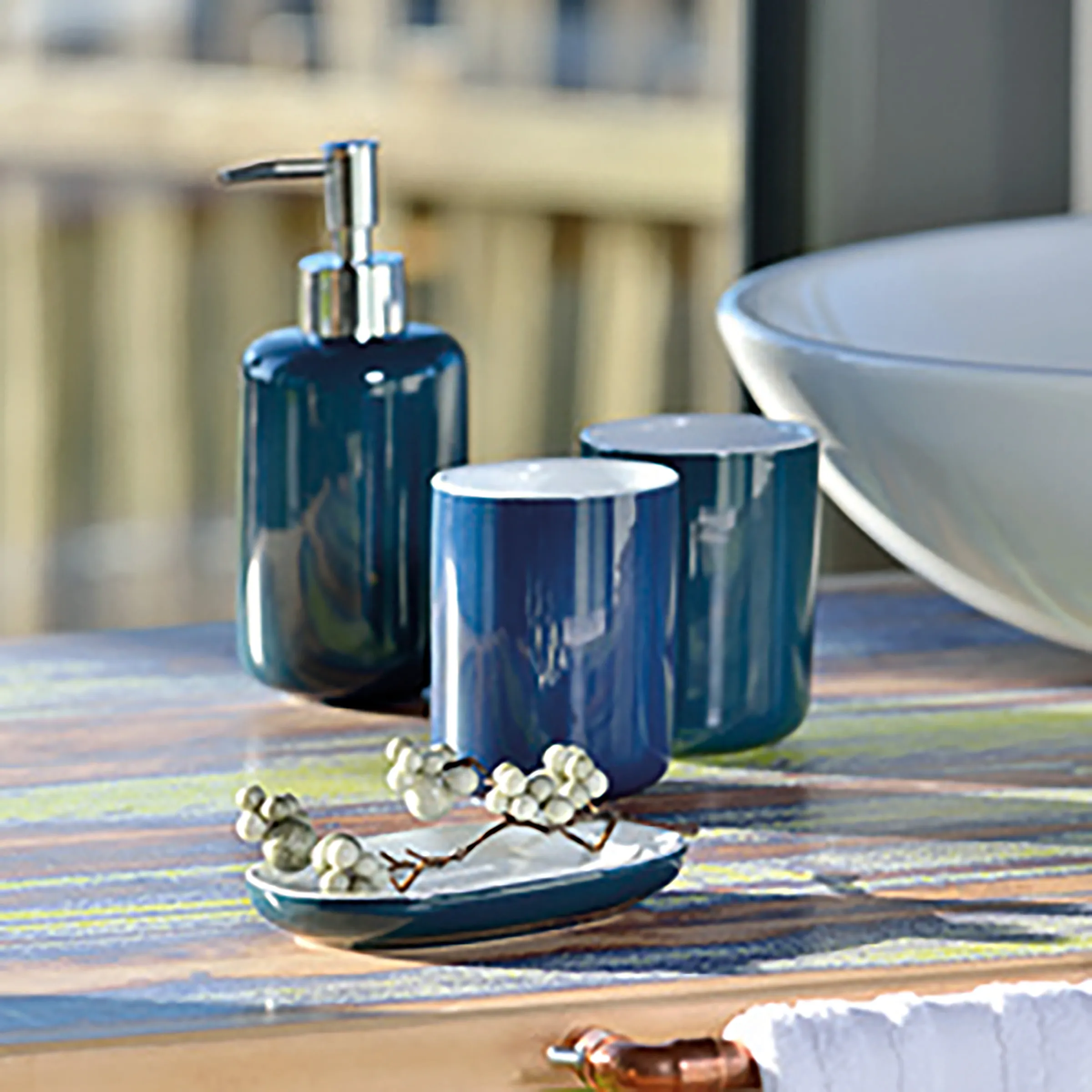 Blaues Badezimmer-Accessoire-Set mit Seifenspender, zwei Bechern und Seifenschale auf buntem Holztisch