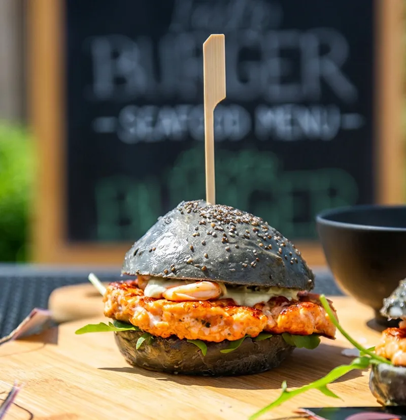 Garnelen-Burger mit schwarzem Sesambrötchen - Gourmet Seafood Gourmet-Burger mit schwarzem Sesambrötchen, würziger Garnelen-Patty, Mayonnaise und grünem Microgreens auf Holzbrett