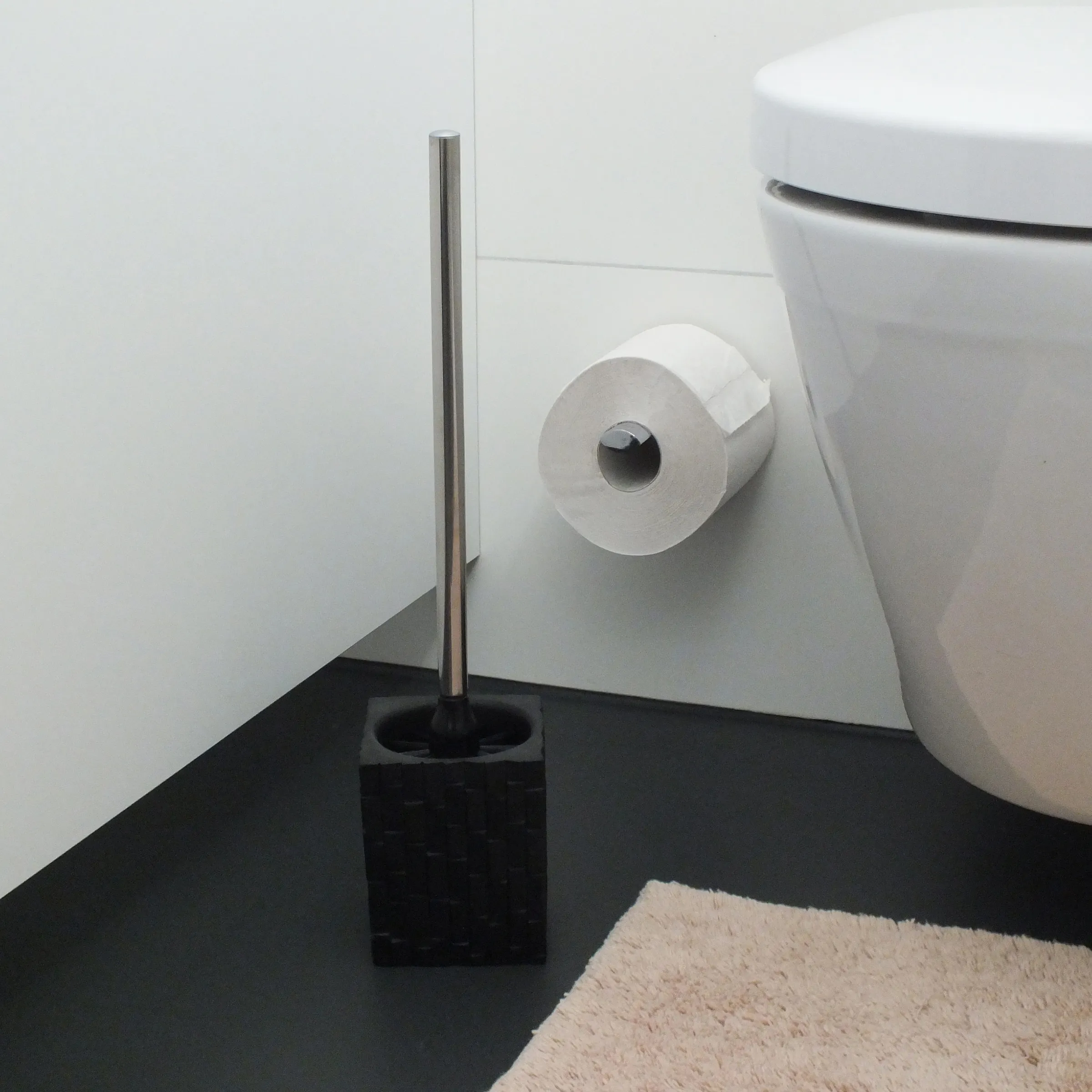 WC-Garnitur Toilettenbürste mit Edelstahl und schwarzem Sockel - Badezimmer Accessoires Moderne Toilettenbürste mit schwarzem Sockel und Edelstahlgriff neben weißer Toilette und Toilettenpapierhalter