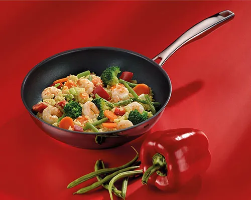 Wok-Pfanne mit Garnelen und Gemüse - Asiakoch Wok mit Garnelen, Brokkoli und Paprika auf rotem Hintergrund mit frischen Gemüsezutaten