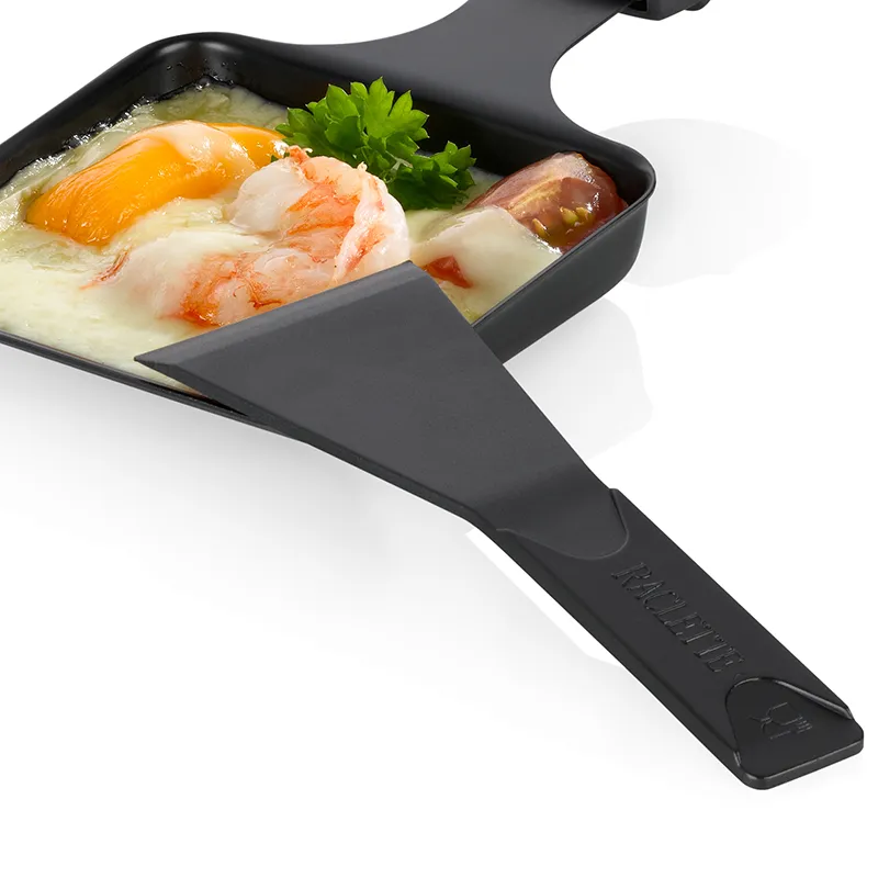 Schwarze Raclette-Pfanne mit Spiegelei, Garnelen und Käse auf weißem Hintergrund