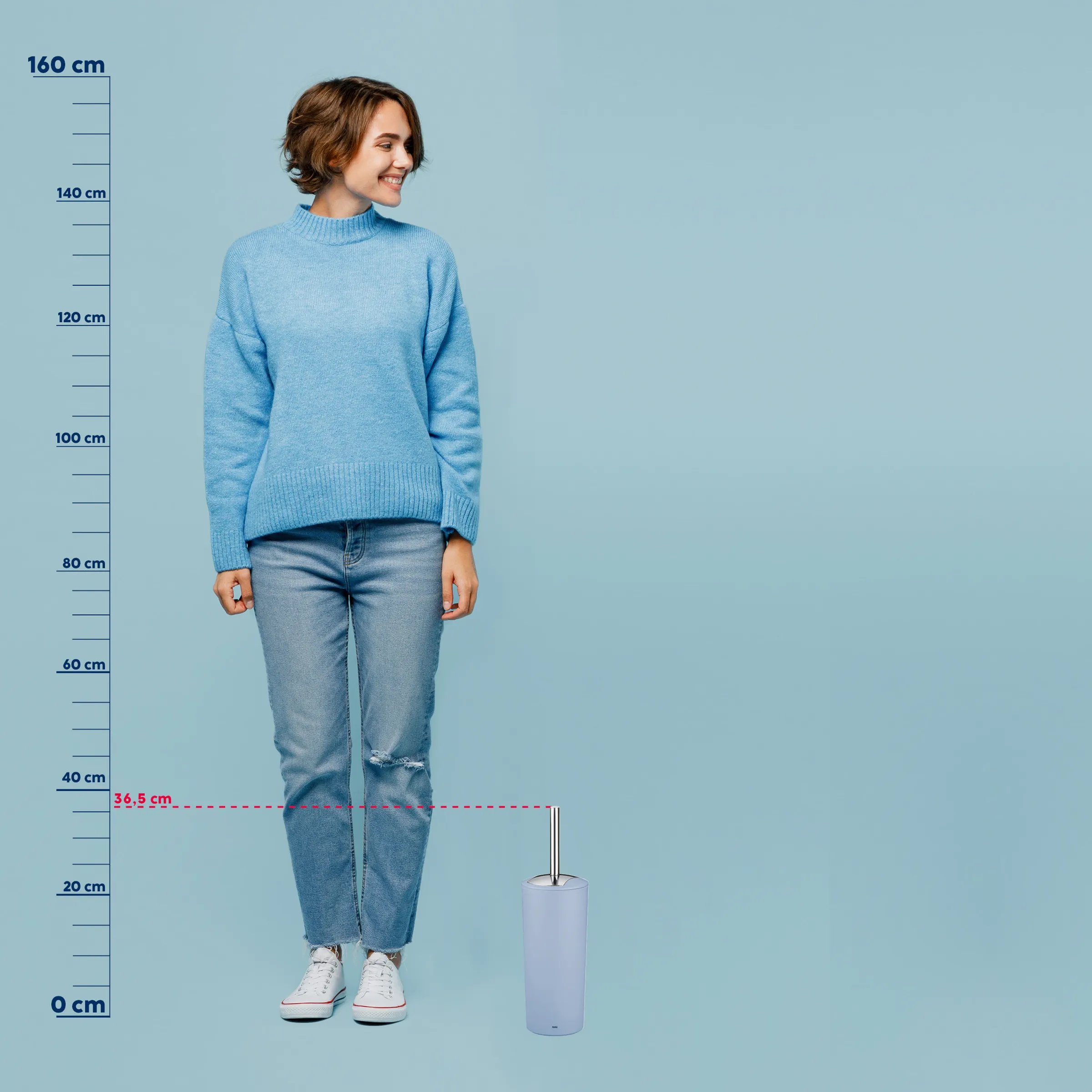 Frau in hellblauem Strickpullover und Jeans neben weißer Toilettenbürste mit Maßstab zur Größenangabe