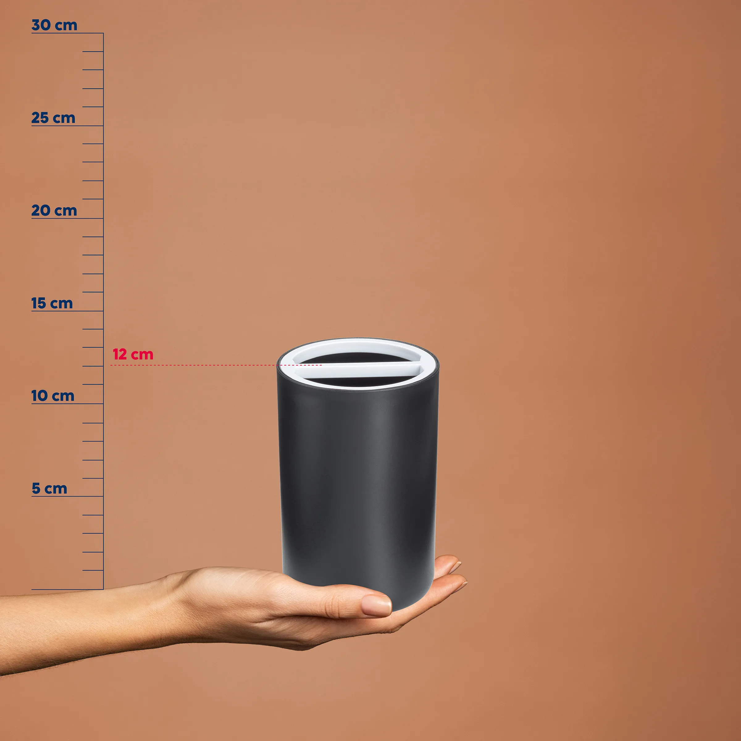Schwarzer zylindrischer Behälter mit Schlitz auf Handfläche, neben Messskala zeigend 12 cm Durchmesser