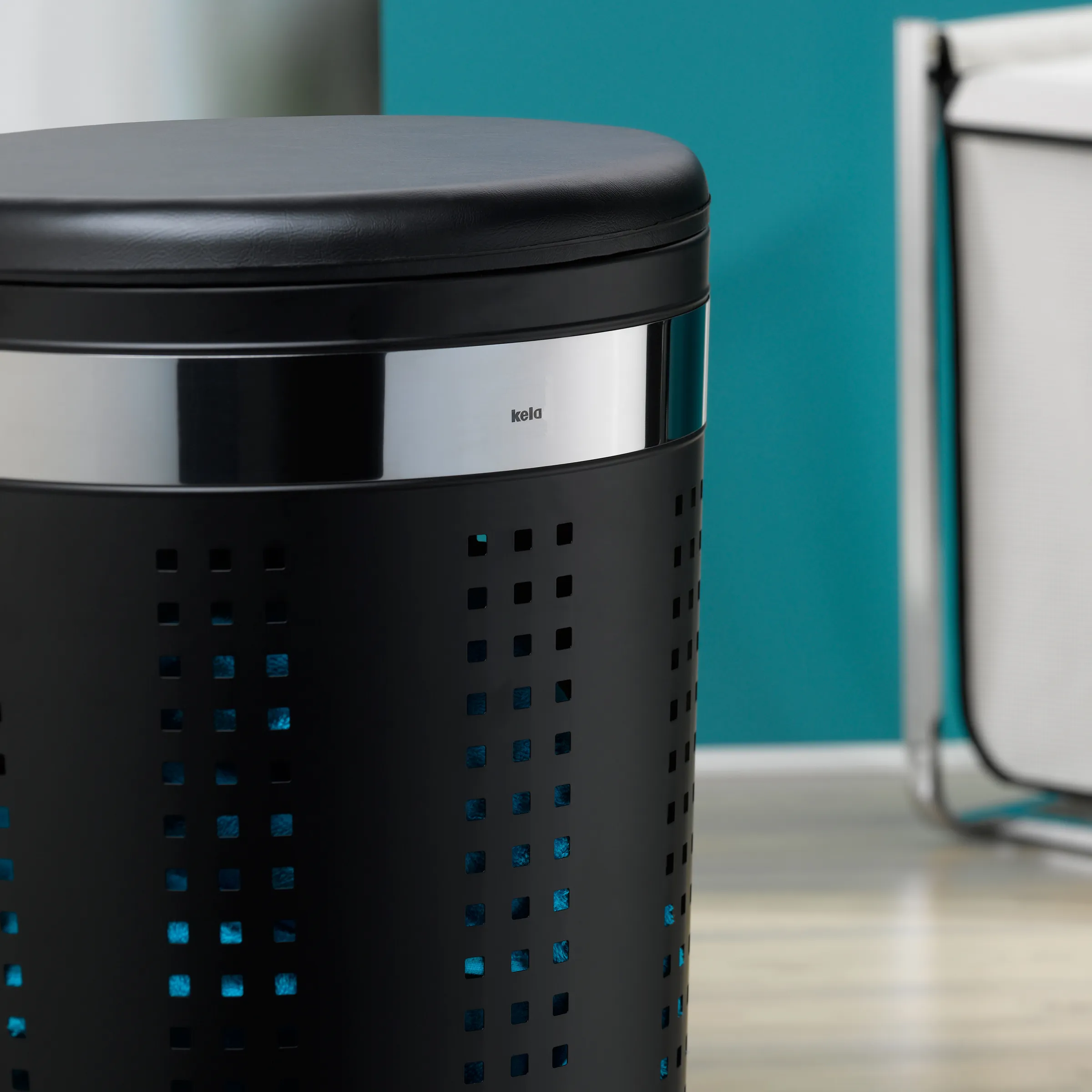 Kela Wäschekorb LED - Design Wäschebehälter mit Licht Schwarzer zylindrischer Wäschekorb mit blauem LED-Muster und silbernem Deckelband auf türkisem Hintergrund