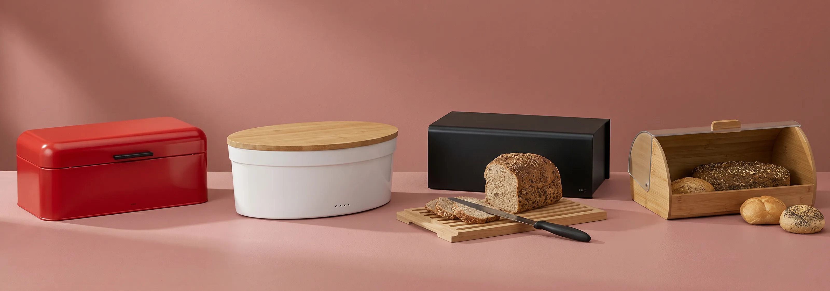 Brotboxen und Brotkasten Set - Moderne Aufbewahrung für Brot und Backwaren Vier verschiedene Brotboxen in Rot, Weiß, Schwarz und Holz mit Brot und Brötchen auf rosa Hintergrund