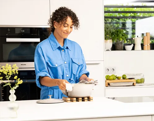 Frau kocht in moderner Küche - Kochen und Rezepte Frau in blauem Hemd kocht in moderner Küche, rührt in Topf, bunte Gewürze und frisches Gemüse auf Arbeitsplatte