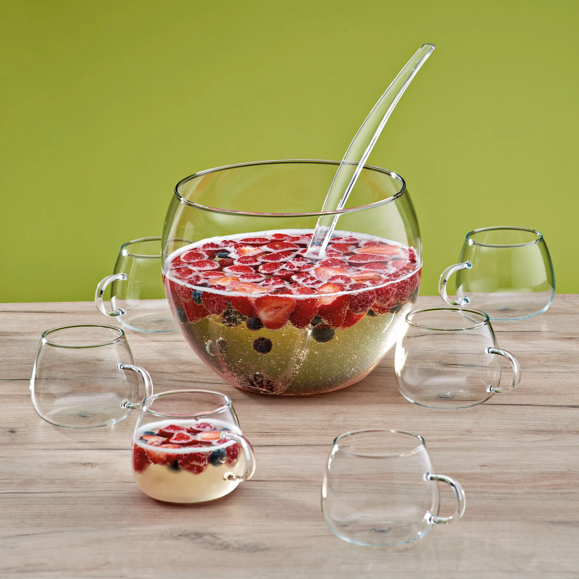Erdbeeren Bowle Set - Glasschüsseln für Getränkeservice Große Bowle mit Erdbeeren, Blaubeeren und Getränk, umgeben von leeren Glasschüsseln auf Holztisch