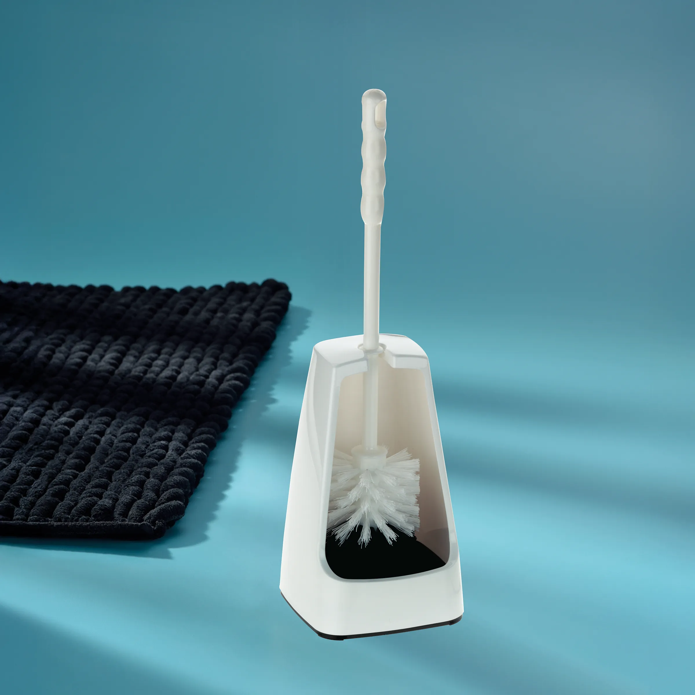 Toilettenbürste mit Halter - Badezimmer WC-Garnitur in Weiß Weiße Toilettenbürste mit Halter auf blauem Hintergrund neben schwarzer Badematte