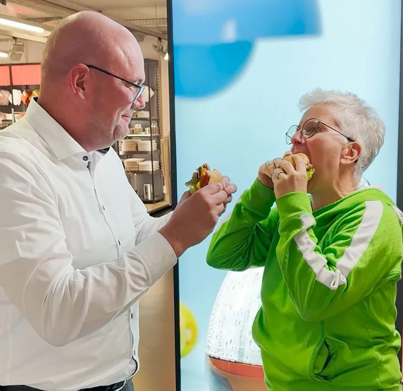 Gesundes Essen: Mann und Frau genießen Sandwiches zusammen Mann in weißem Hemd und Frau in grüner Jacke essen gemeinsam Sandwiches vor blauem Hintergrund