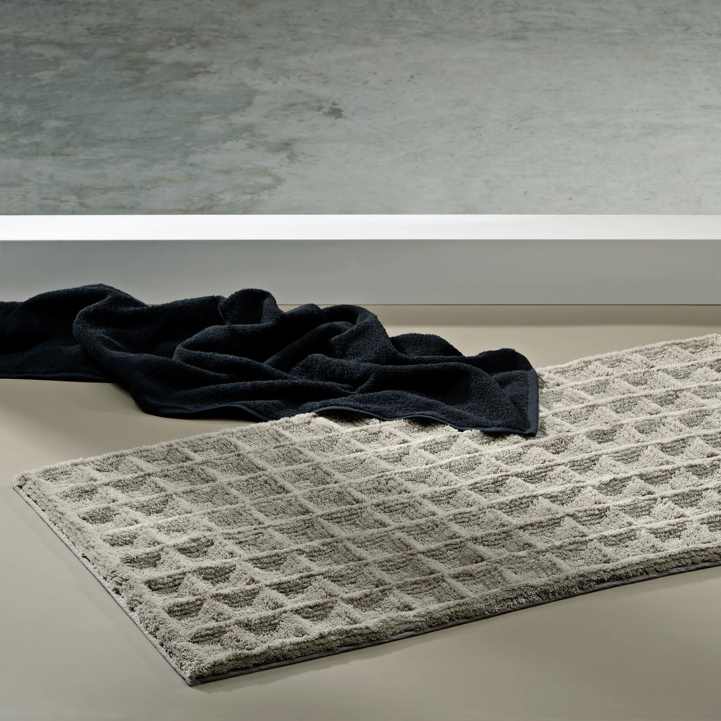 Badezimmer Handtuch Set - Beige Waffelpiqué Beige strukturiertes Badezimmer-Handtuch auf grauem Boden neben schwarzem Stoff, minimalistische Produktpräsentation
