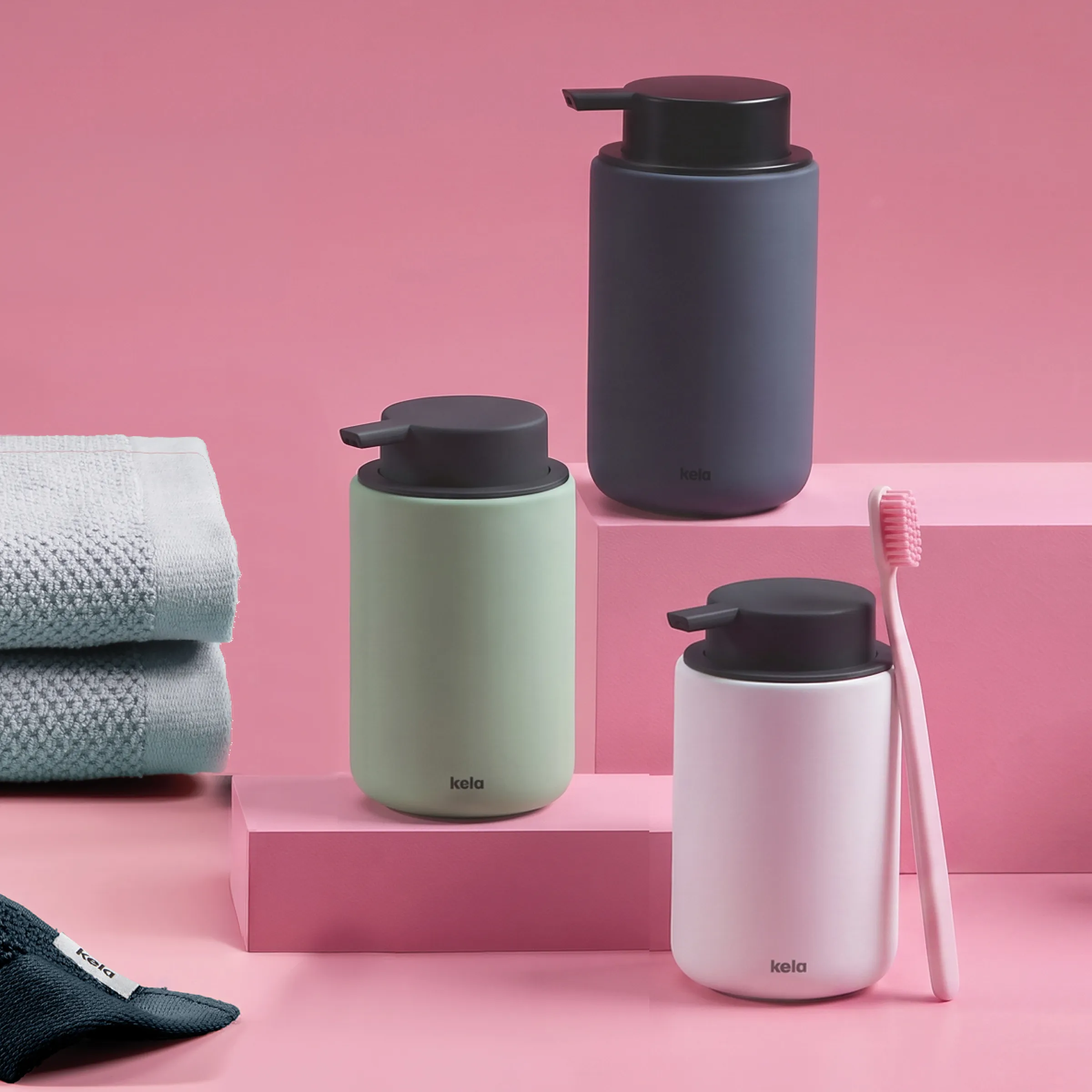 Ensemble Kela distributeur savon - accessoires salle de bain modernes Distributeurs de savon Kela et brosse à dents en différentes couleurs sur fond rose avec serviettes et accessoires